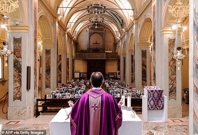 Pictured: Don Giuseppe Corbari, parson of the Church of Robbiano, holds Sunday mass as he looks towards selfie photographs sent in by his congregation members and glued to empty pews in Giussano on March 22, 2020