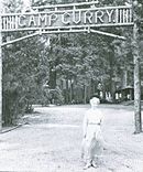Женщина в длинном платье перед знаком через дорогу.  Деревянные буквы читать «Camp Curry».