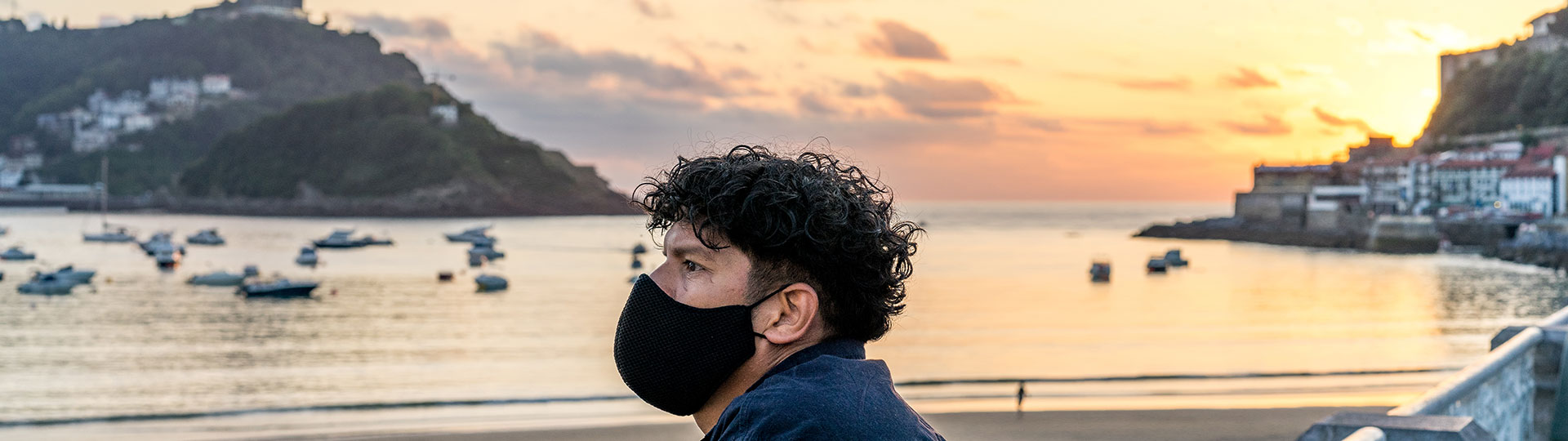 Boy with mask looking at the sunset on La Concha beach, San Sebastian