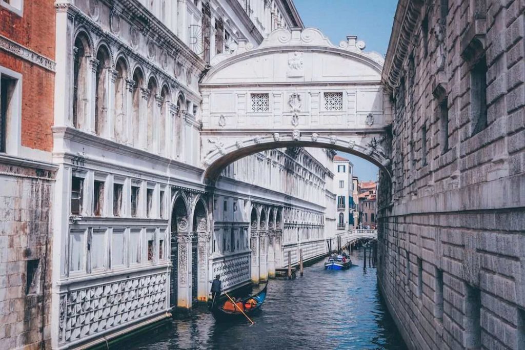 gondolas paddle along a canal in venice with an arch 